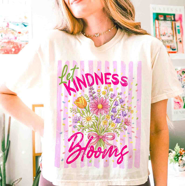 Person wearing a white t-shirt with 'Let Kindness Bloom' design featuring flowers and text.